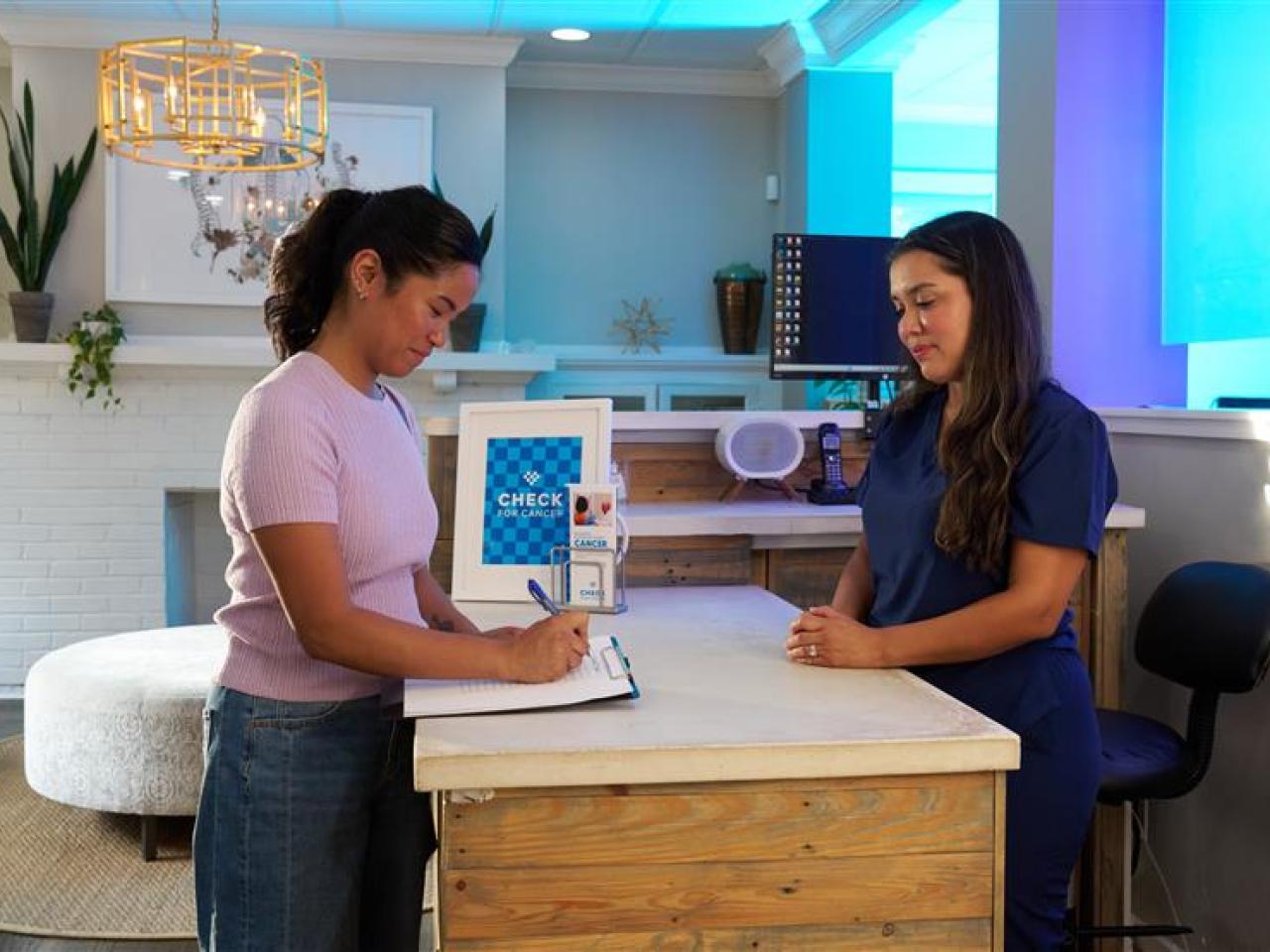 A person filling out a form at a clinic with another person behind a desk.