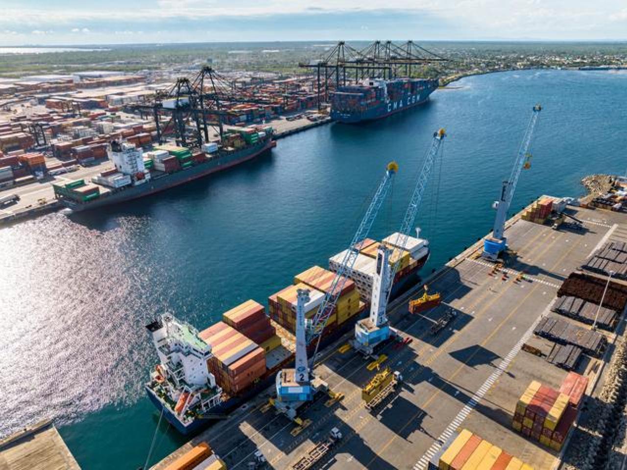 Aerial view of DP World port operations in the Caribbean, showing cargo vessels, cranes, and stacked shipping containers along the quay.