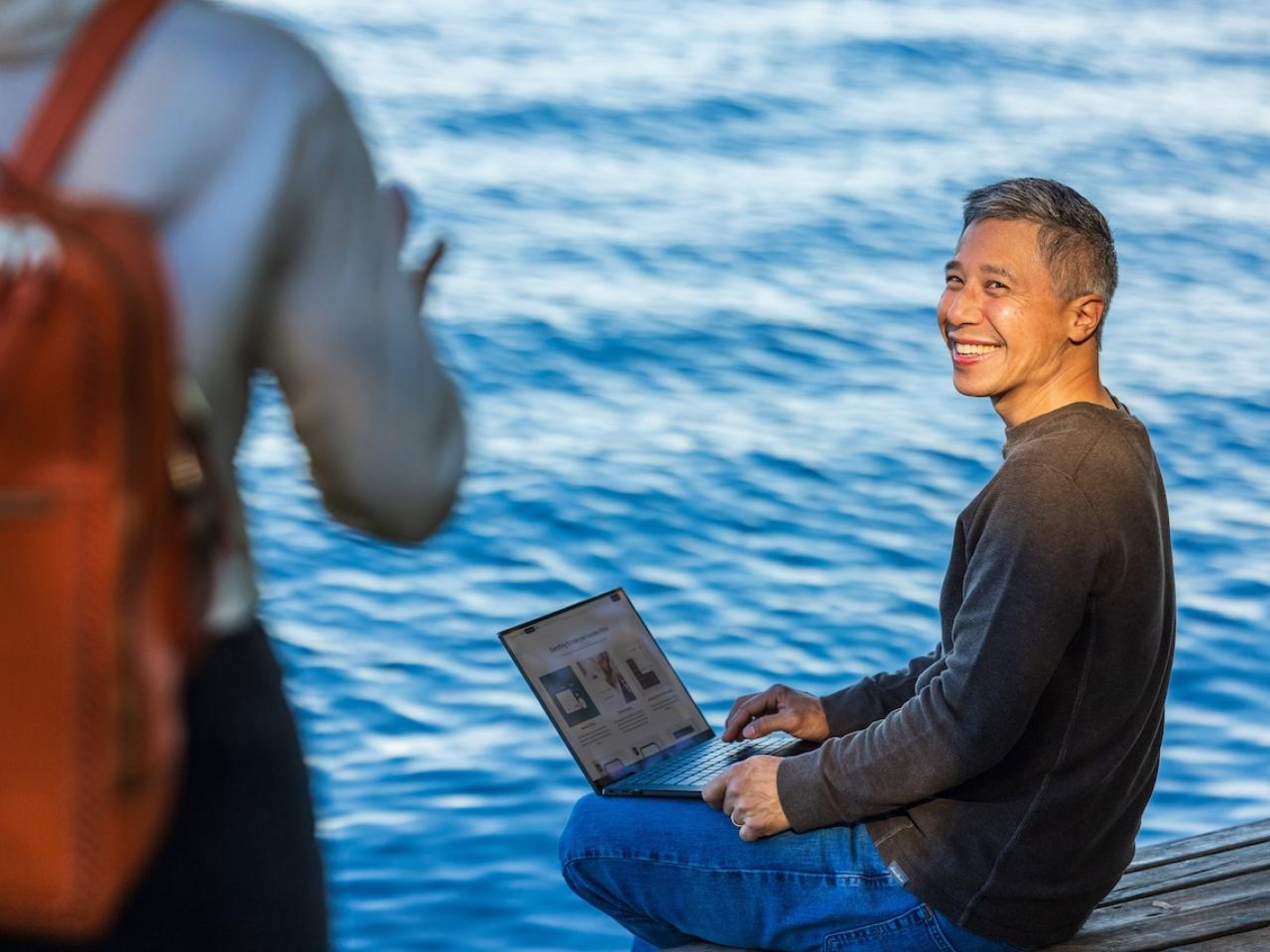 Person on a laptop seated next to a lake.