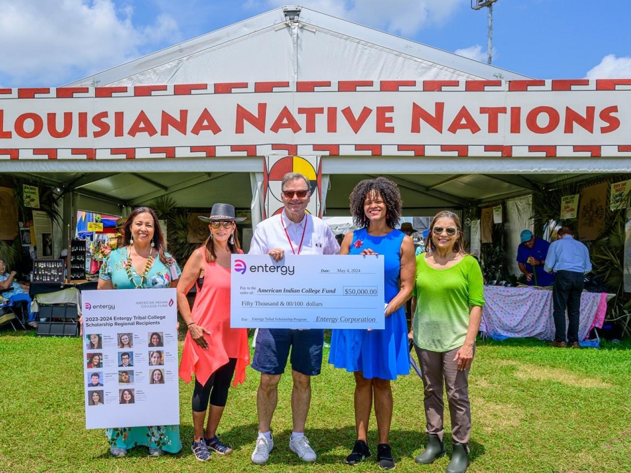 Five people posed with a large check and profiles of scholarship winners posed outside a booth "Louisiana Native Nations."