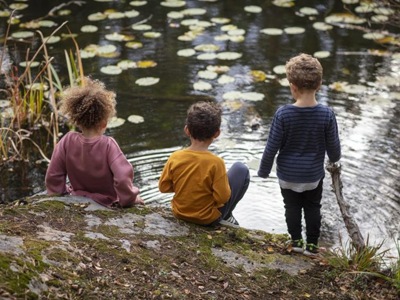 Three children sitting by a stream.