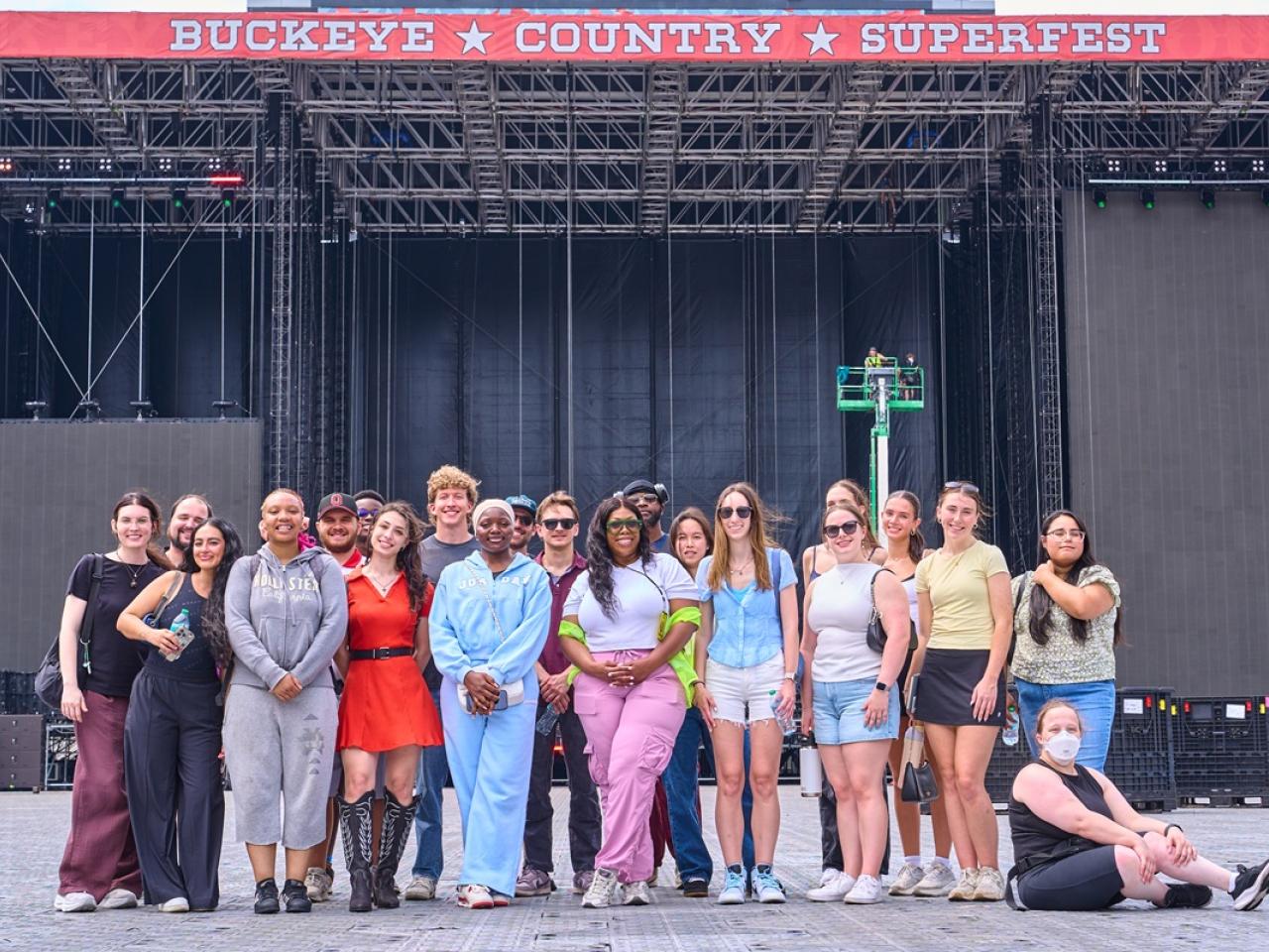 College program participants pose for a group photo in front of the main stage at Buckeye Country Superfest, standing on the festival grounds before the event begins.