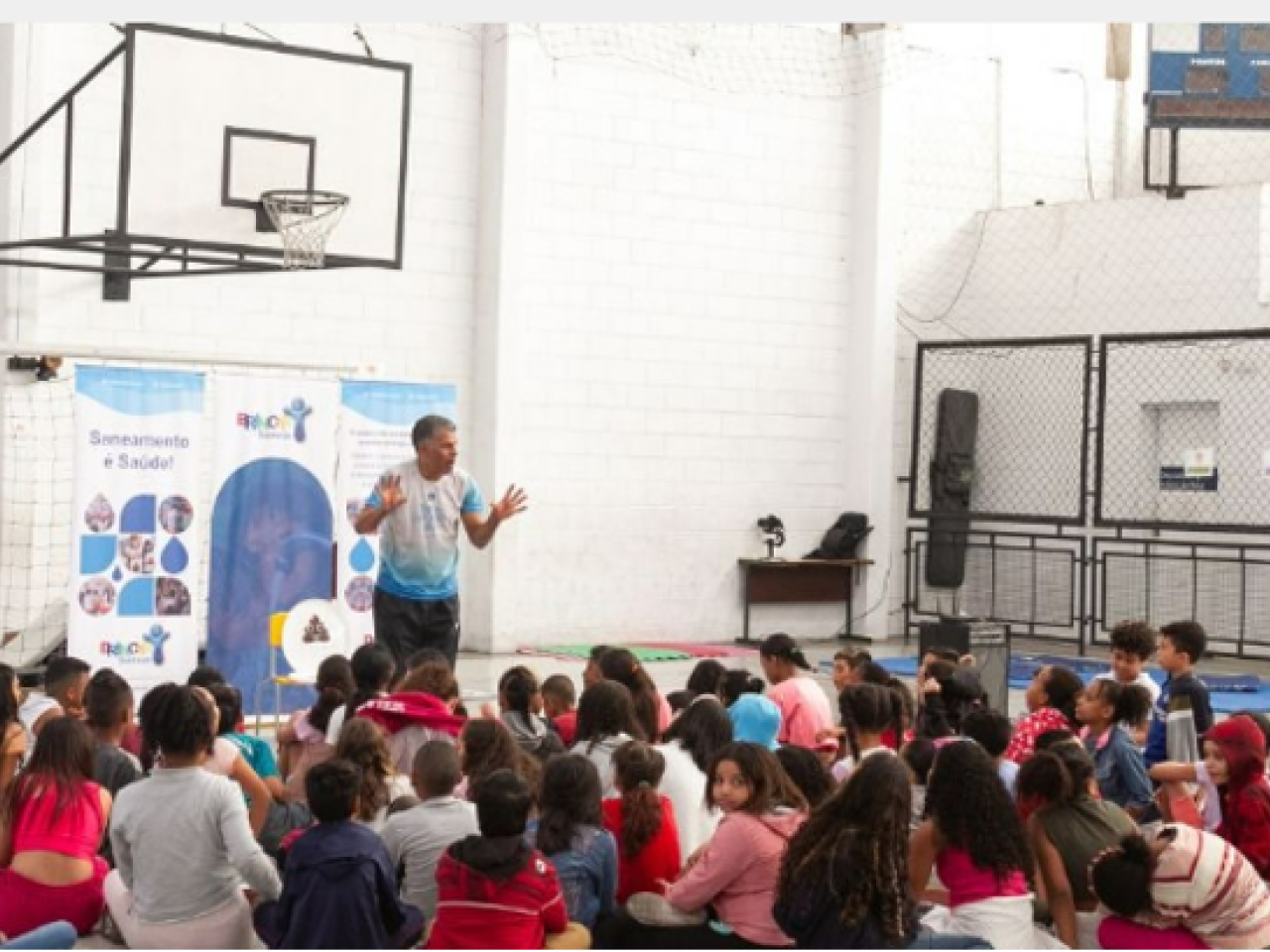 Person stood in a hall giving a presentation to students who are sat on the floor in front of them