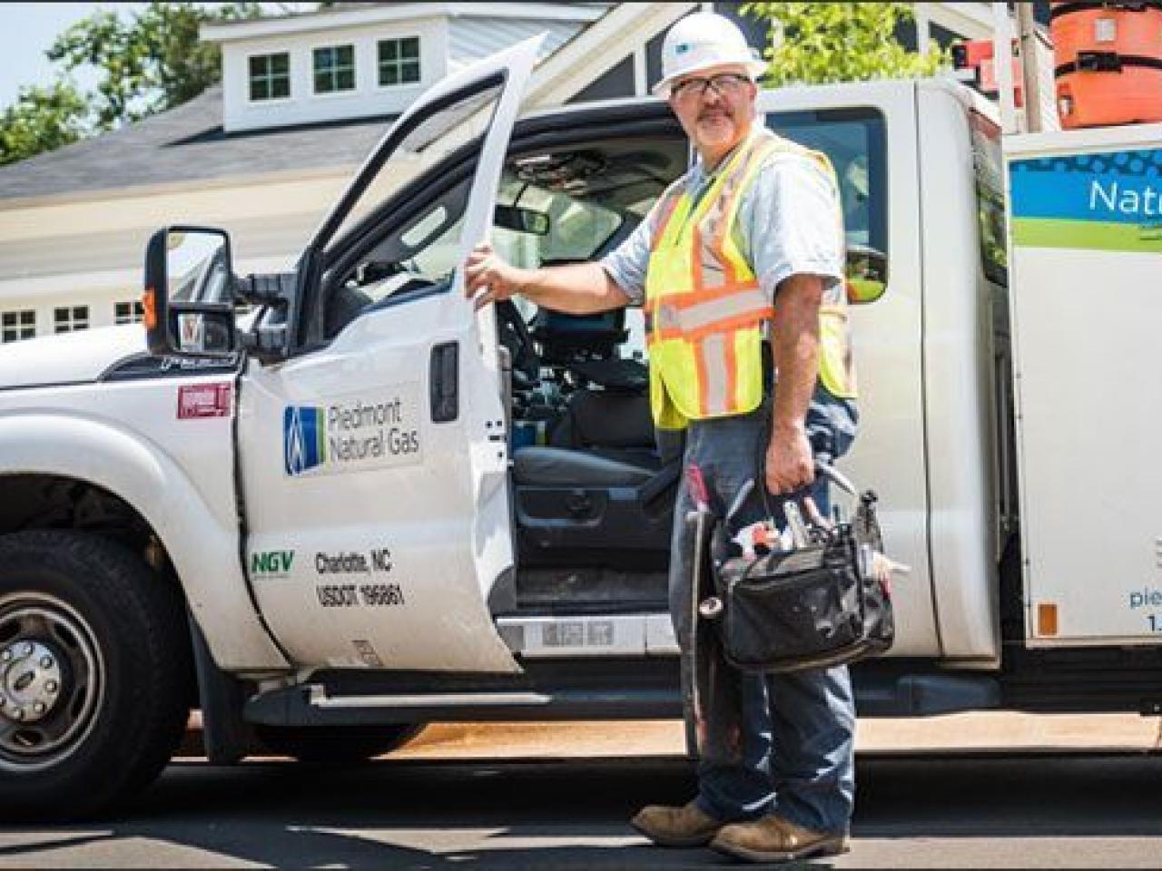 A utility worker standing with a hand on an open door to a utility truck in a residential area.
