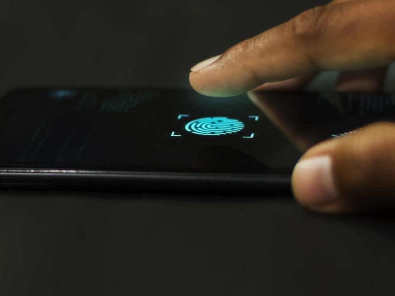 A close-up of a finger poised to tap a fingerprint scanner icon on a smartphone screen, indicating biometric authentication.