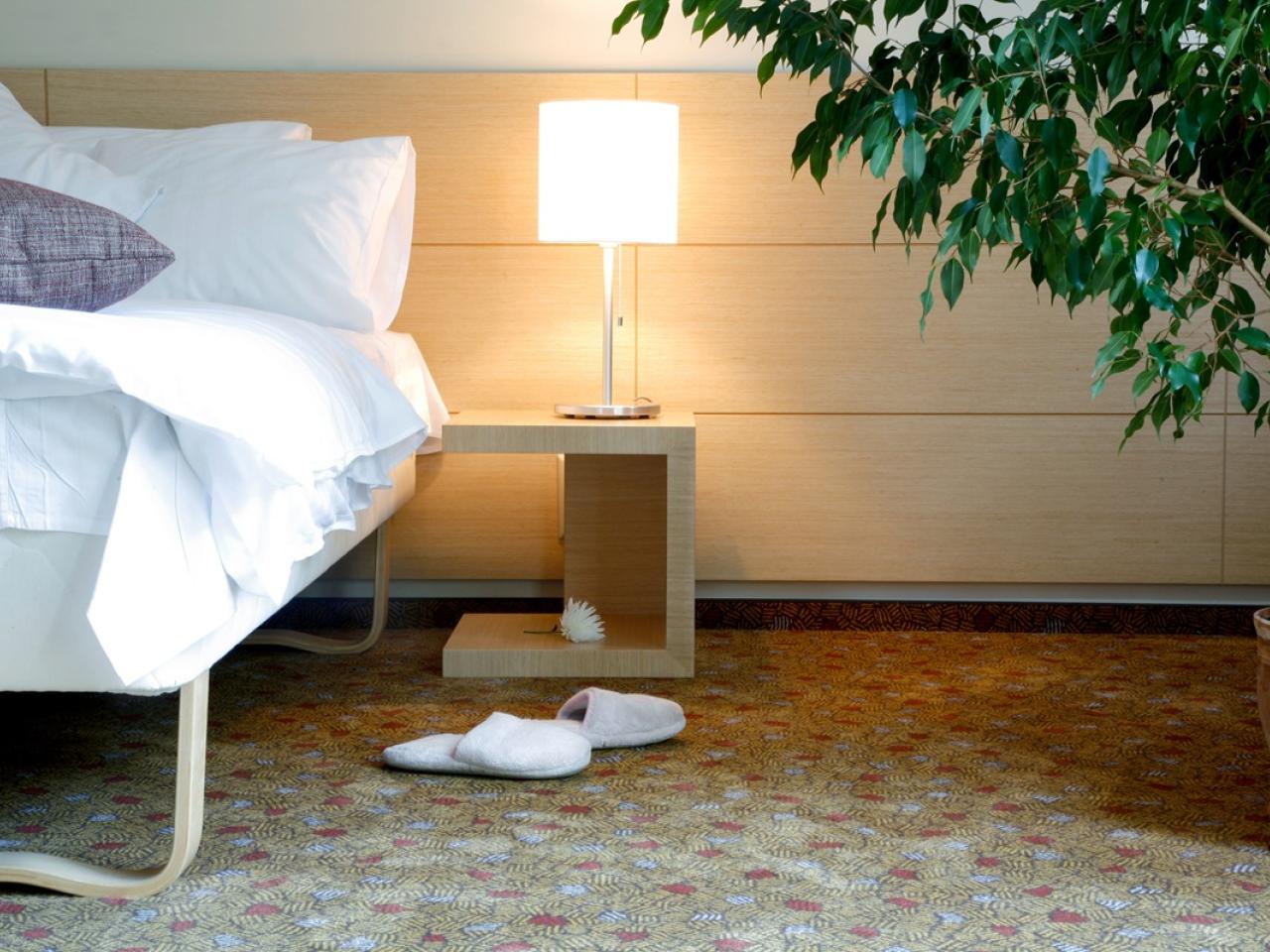 Horizontal view of a hotel room with a bed, side table, lamp, and slippers