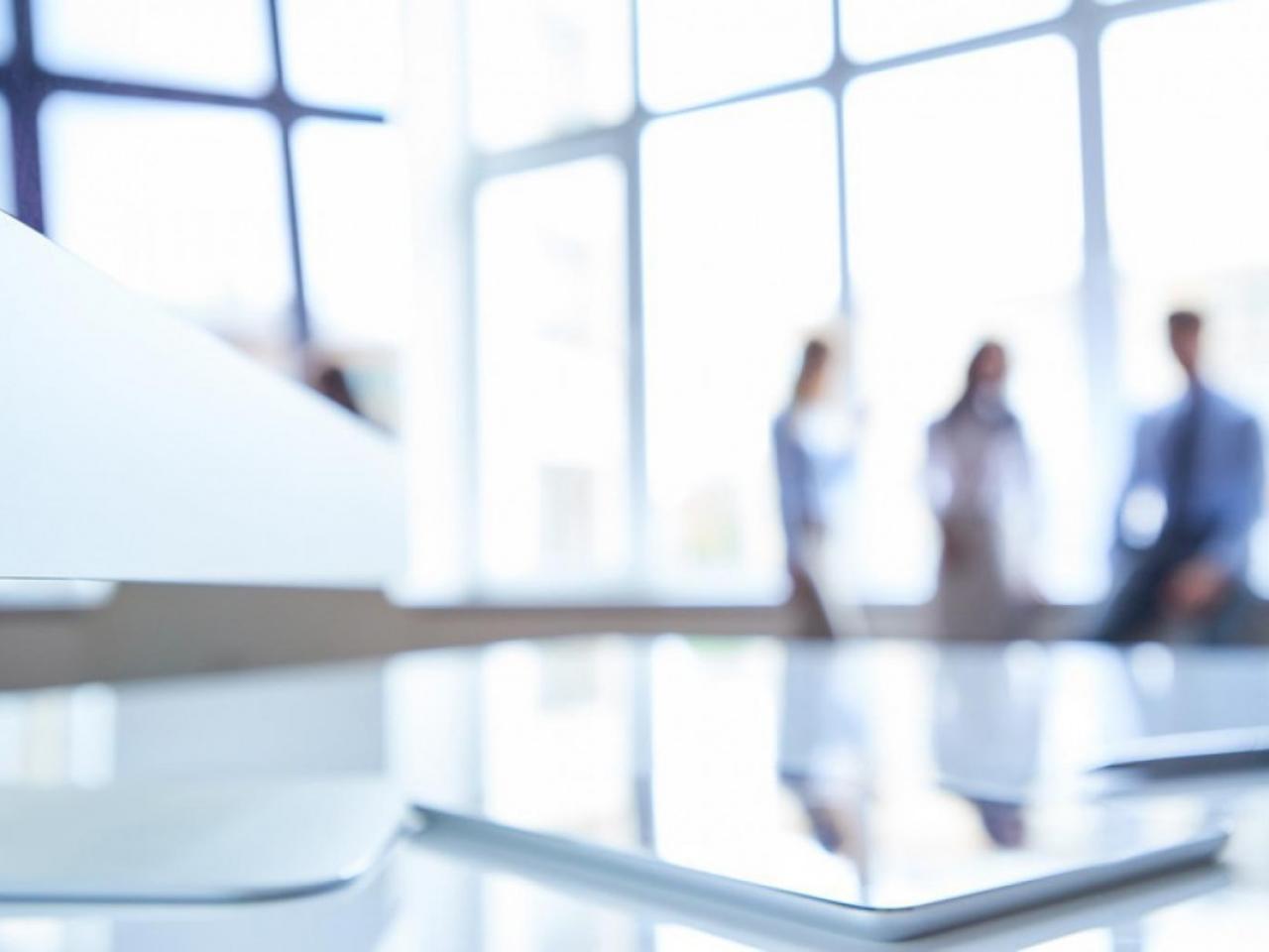 Blurred photo featuring three people in the back of a well-lit office space