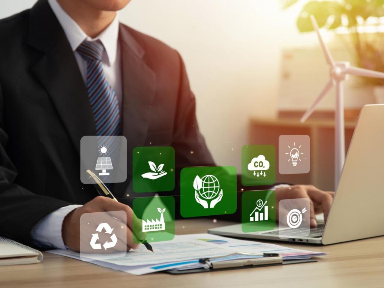 Business employee working at desk with sustainability related symbols in foreground