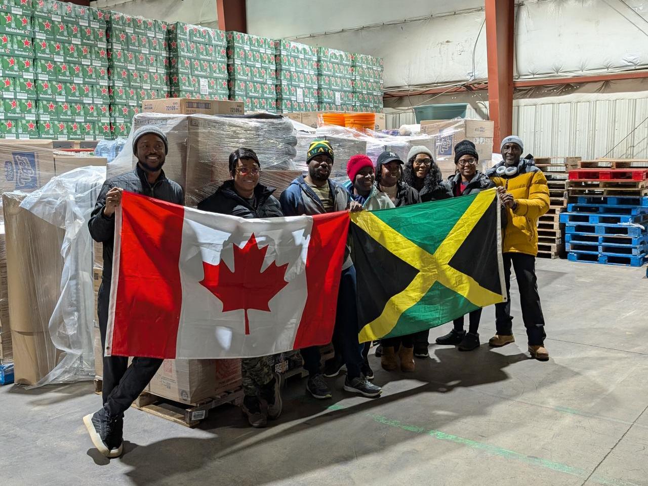 DP World employees and local volunteers stand inside a warehouse holding Canadian and Jamaican flags in front of palletized relief supplies bound for hurricane-affected communities in Jamaica.