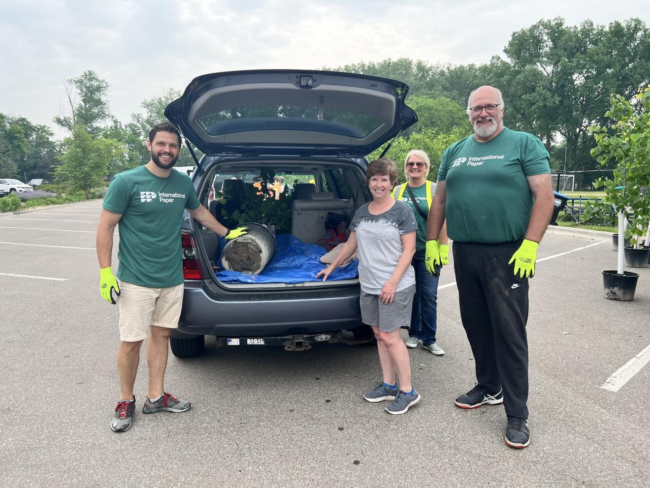 People stood next to a car that has the boot open and a plant inside