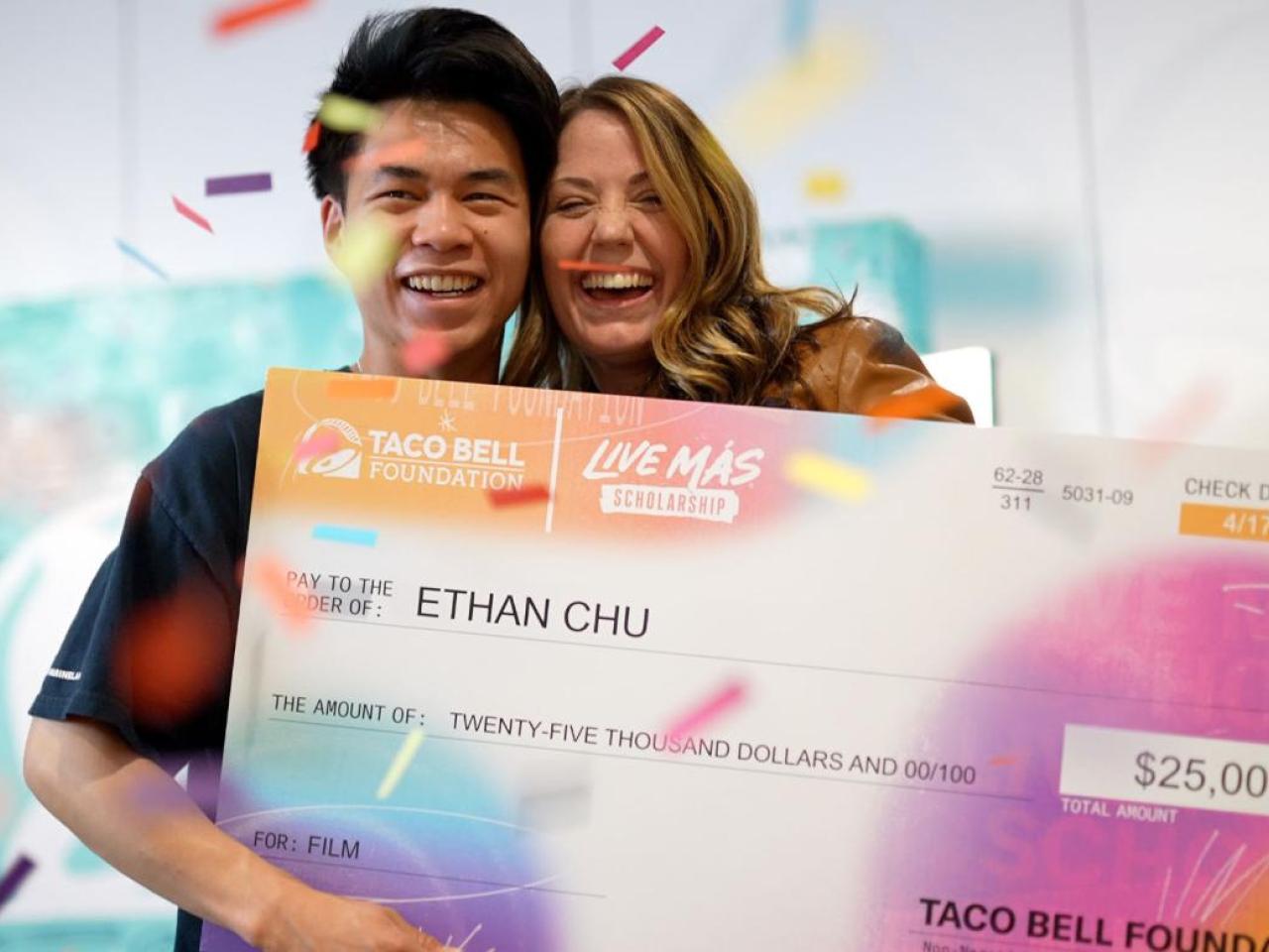 Two smiling people posed with a large check. Confetti falling around them.