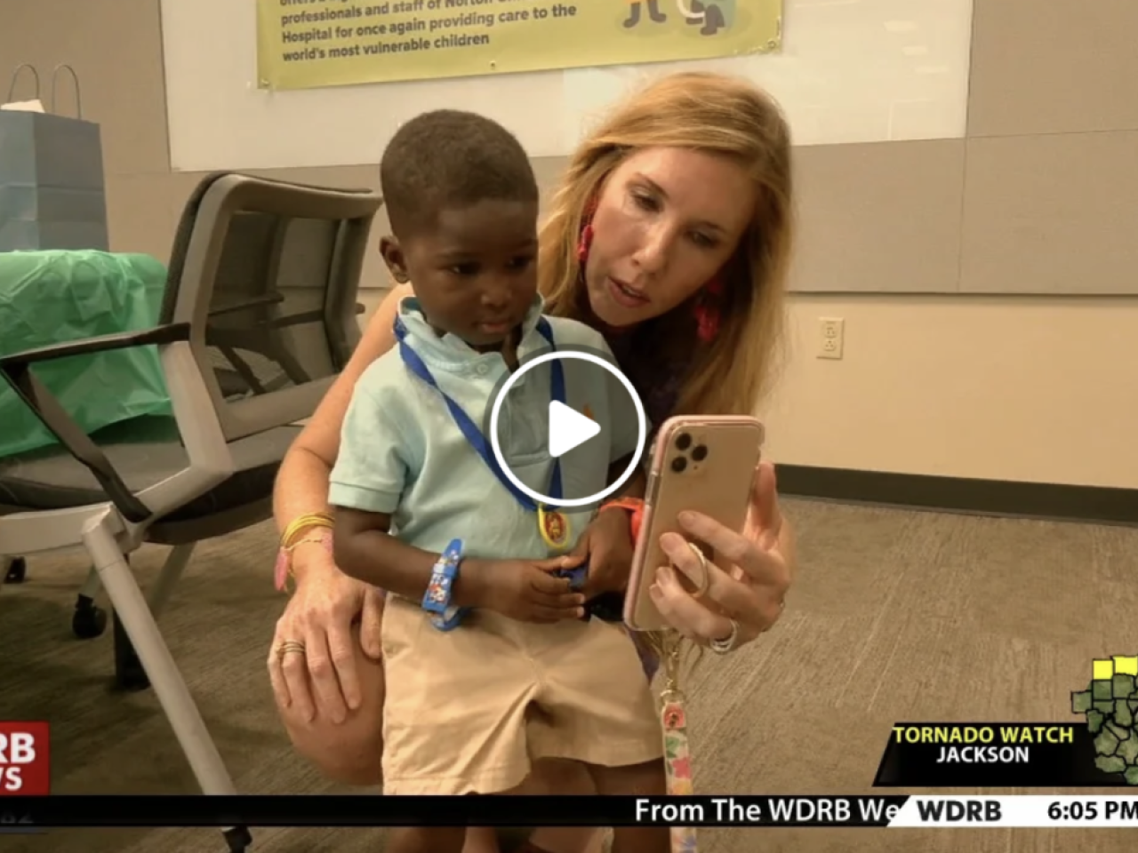 A woman holds up a phone for a child in a light green shirt