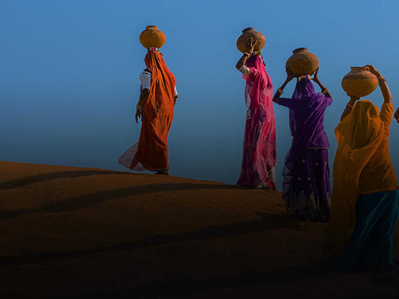 Women carrying pots of water across a desert.