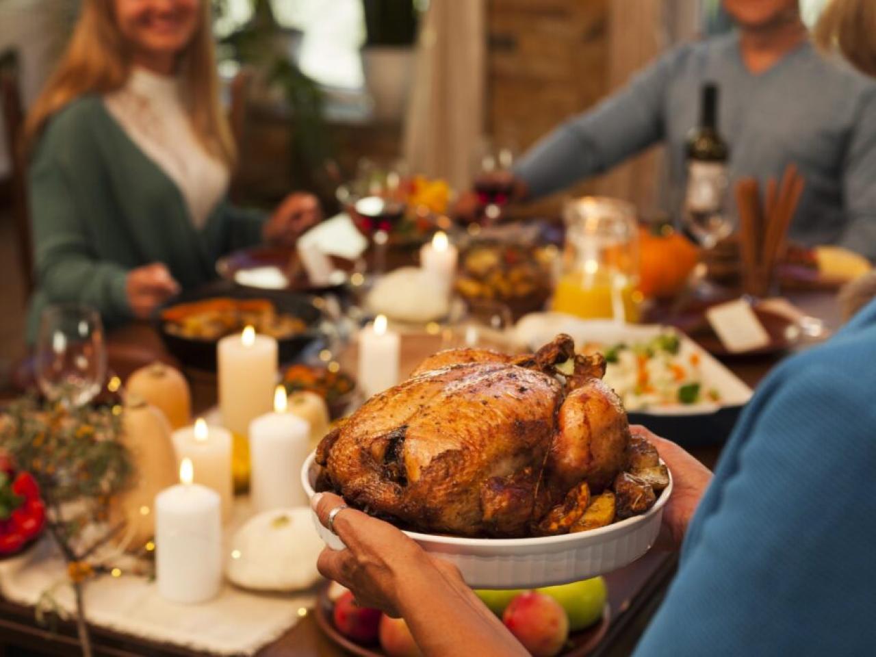 Thanksgiving dinner table with guests and a turkey are shown.