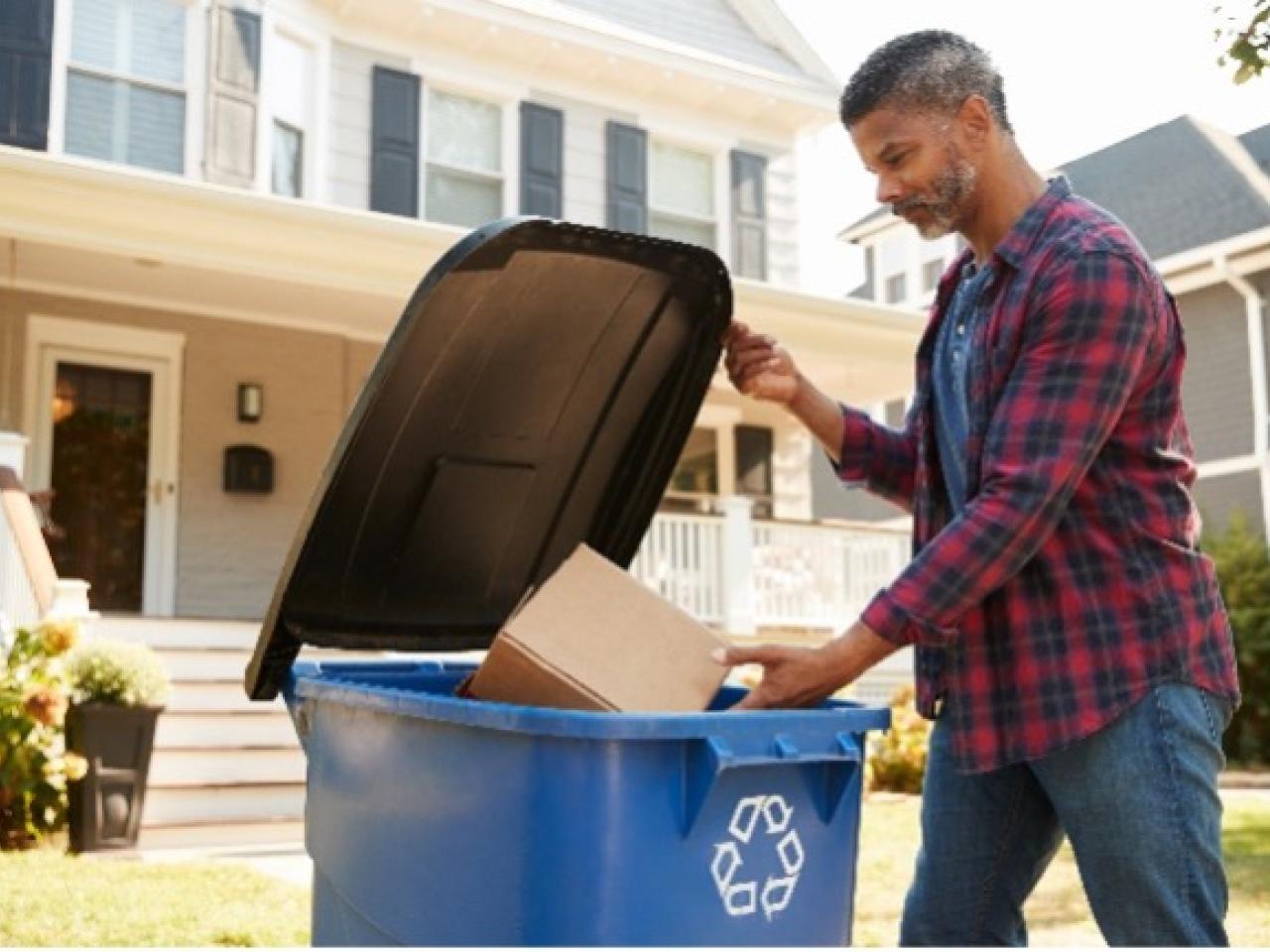 person putting box in recycling bin