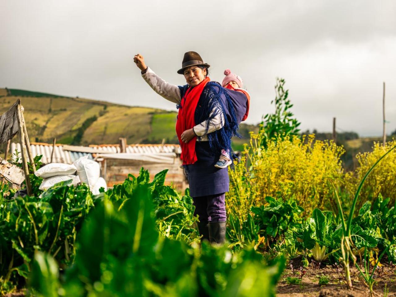 farmer stands in a field her baby strapped to her back
