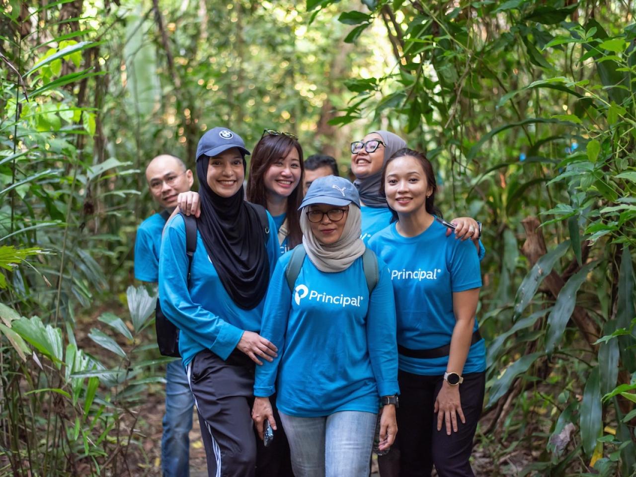 Group of people wearing blue Principal Financial Group shirts in a forest.