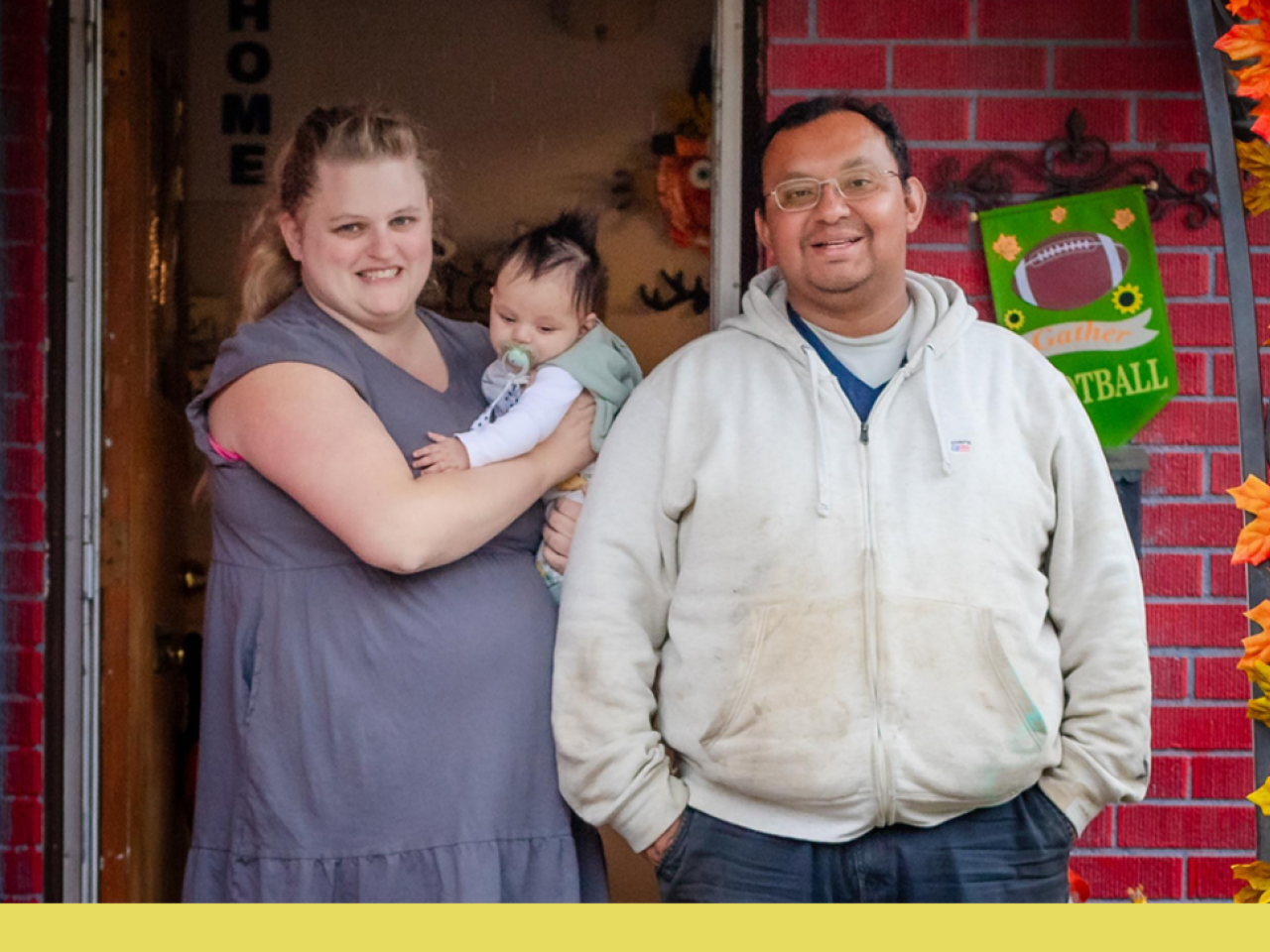 A smiling couple on their porch holding a baby