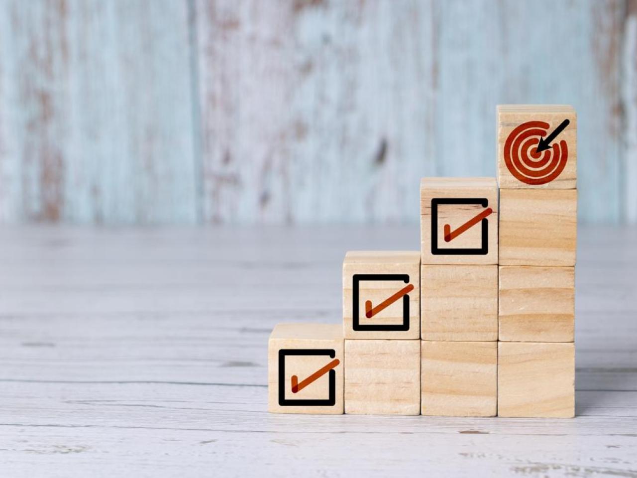 Wooden blocks with checked boxes stacked to mimic four steps