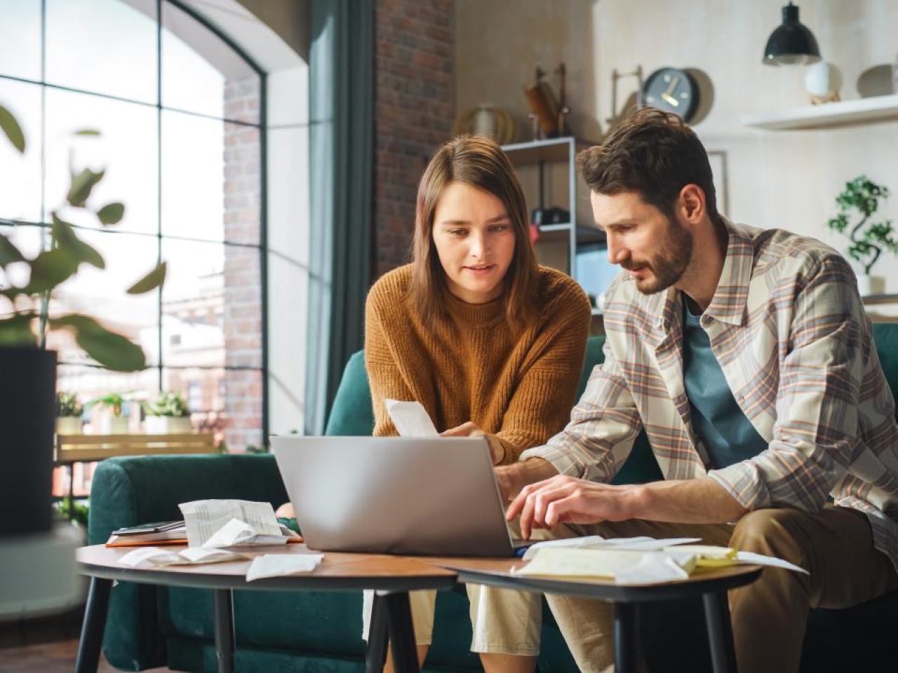 A young couple seated on a couch in front of a laptop.