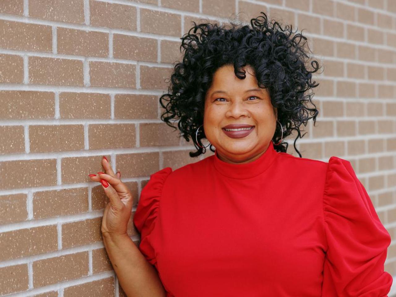 Stacey Bledsoe in a red shirt leaning against a brick wall.