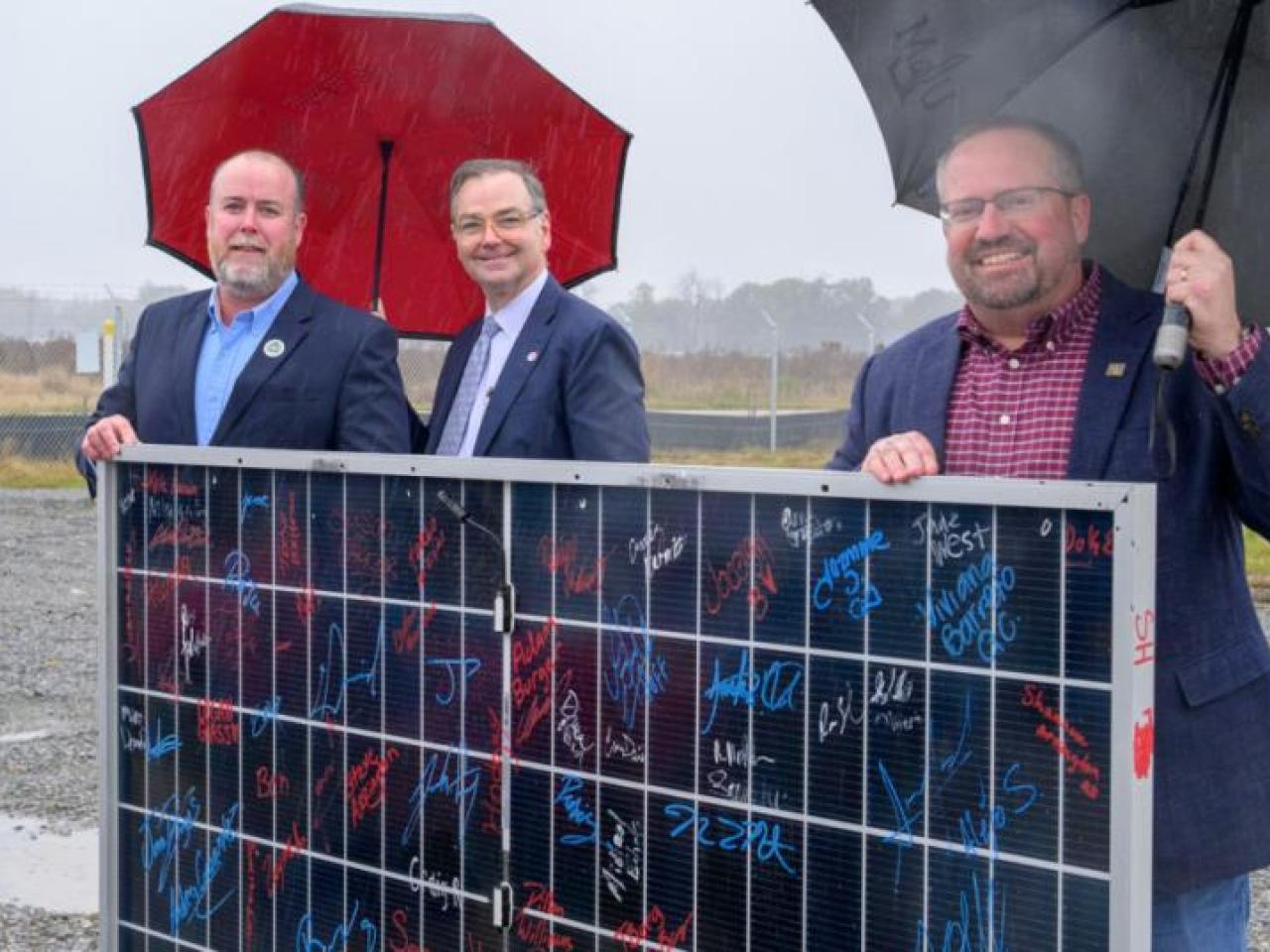 Three men holding umbrellas at opening of facility