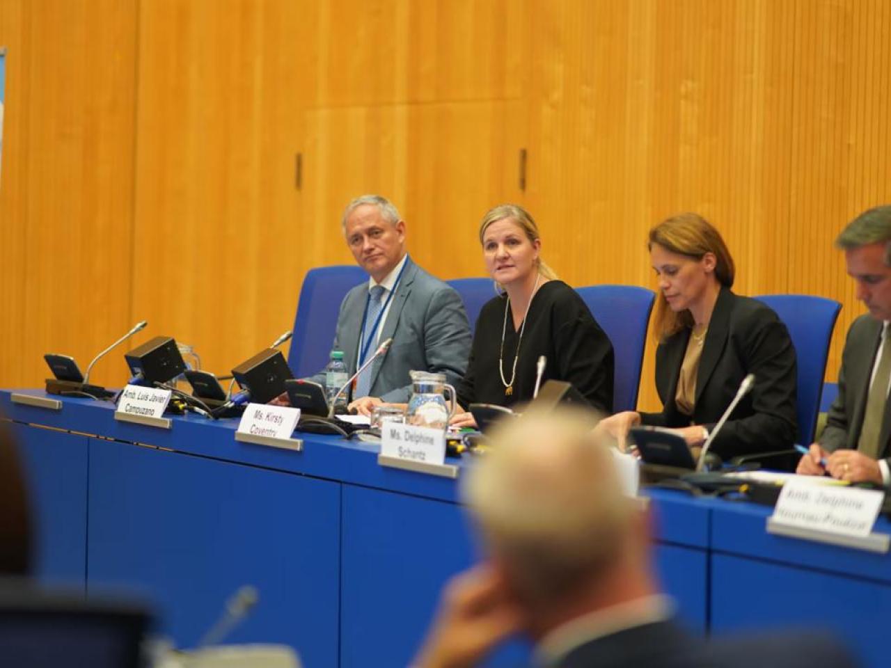 A panel of four at official desks.