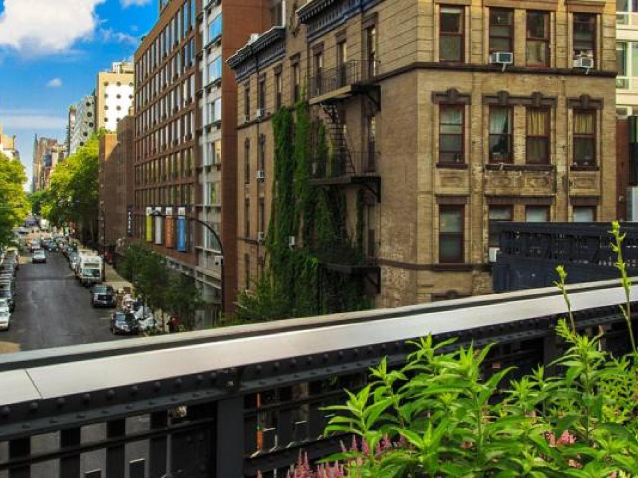 Panoramic view of an urban city with tall, close buildings. An elevated train line running through it. Greenery on the side.