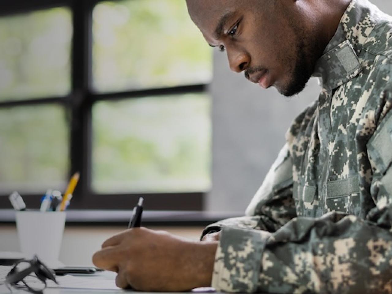 Male military individual seated at a desk wearing fatigues.