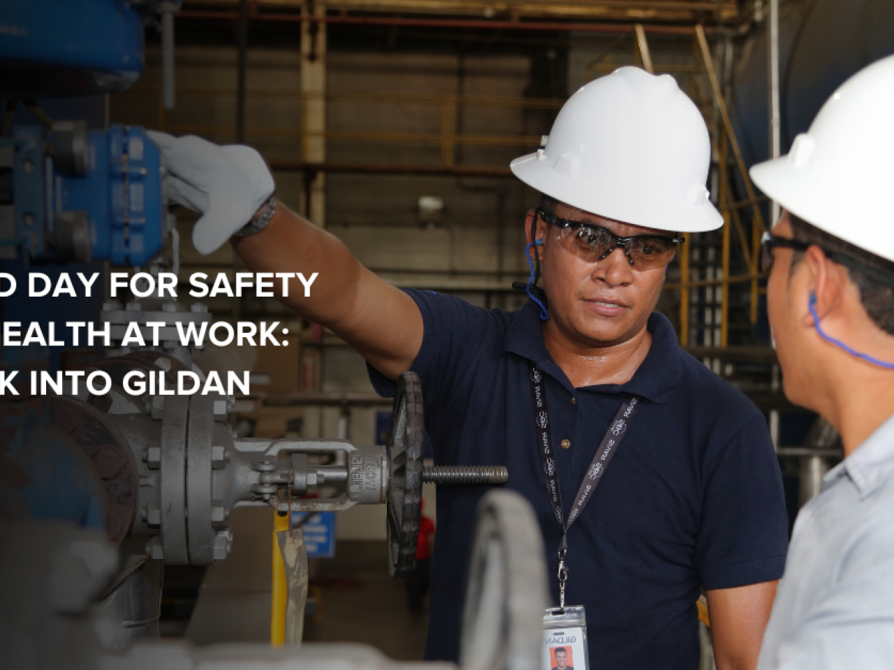 Two Gildan employees wearing safety equipment, interacting on the factory floor