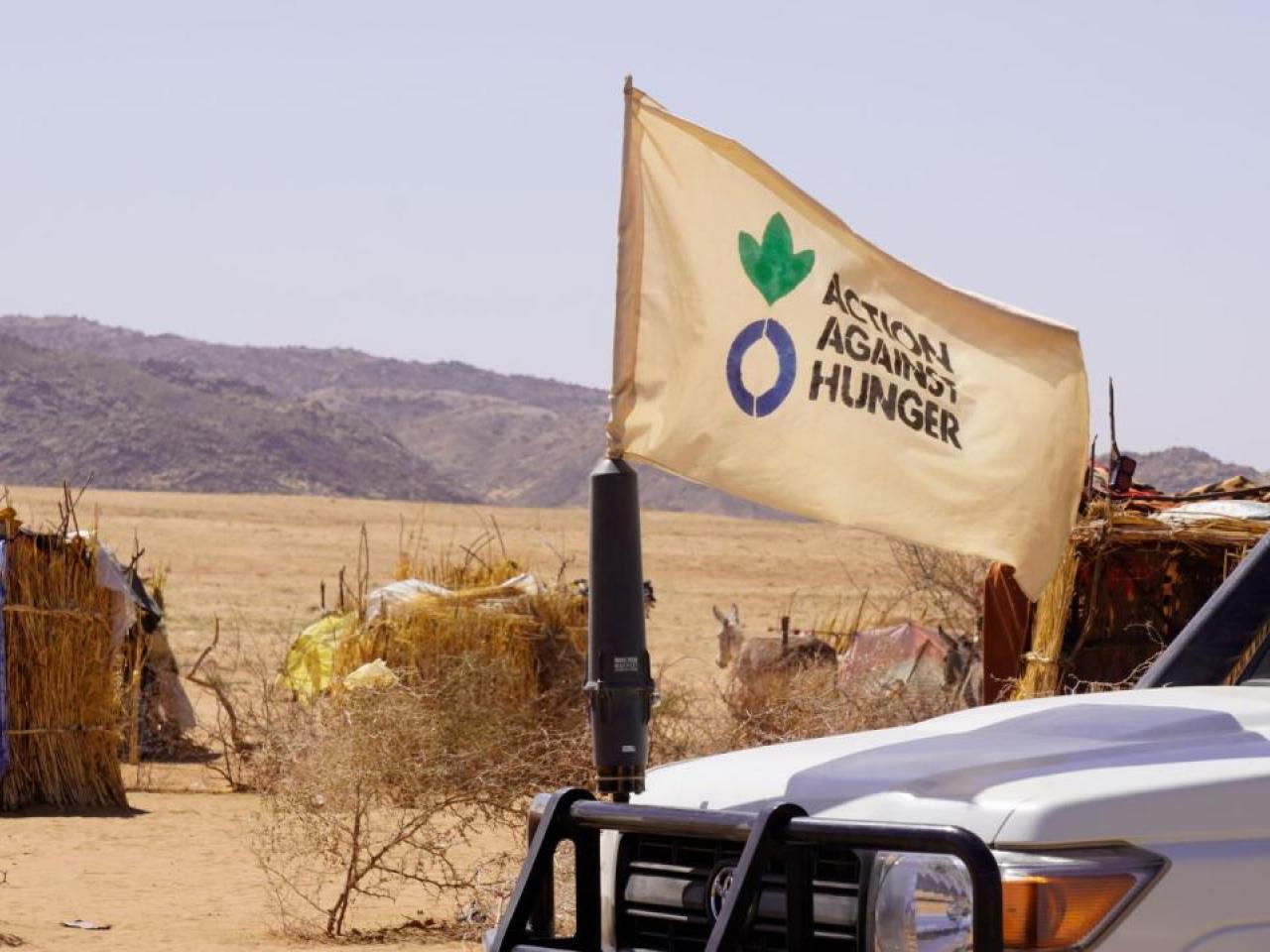 Action Against Hunger flag waves in front of vehicle.