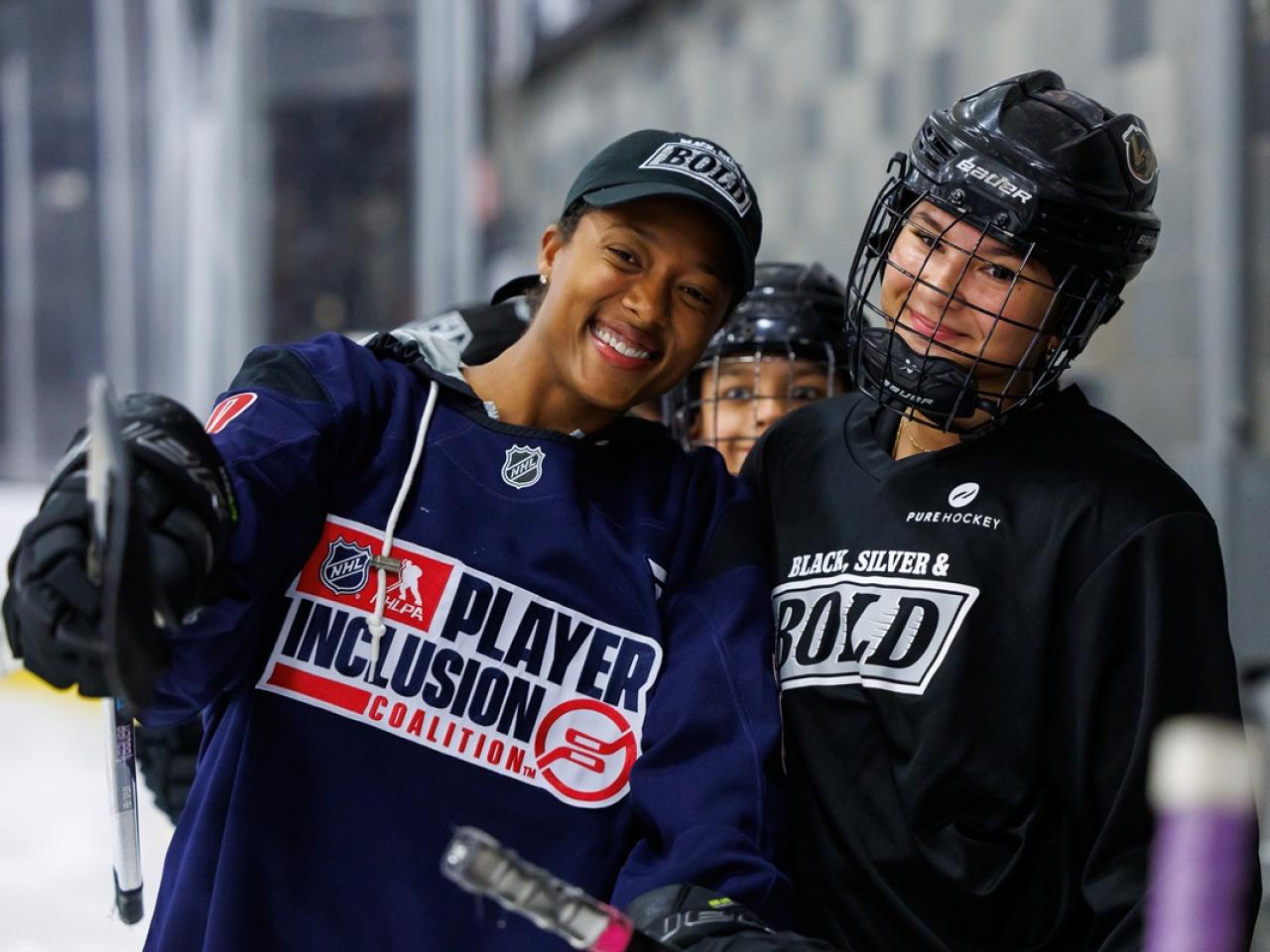 Blake Bolden in a Player Inclusion Coalition jersey poses with a participant in Black, Silver & Bold gear during a hockey clinic.