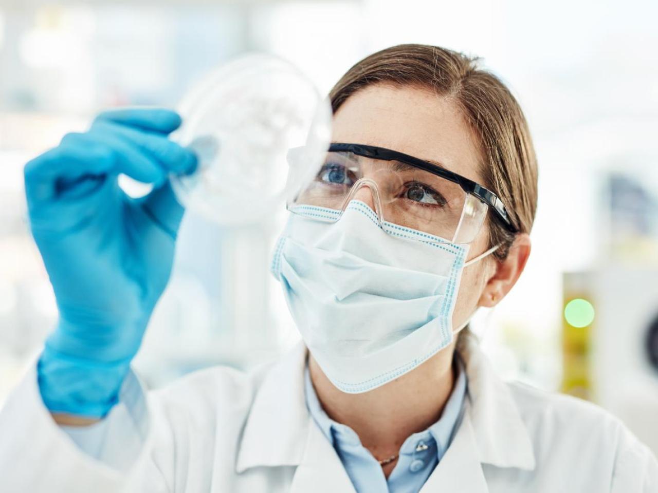 A scientist in protective gear looking at a petri dish
