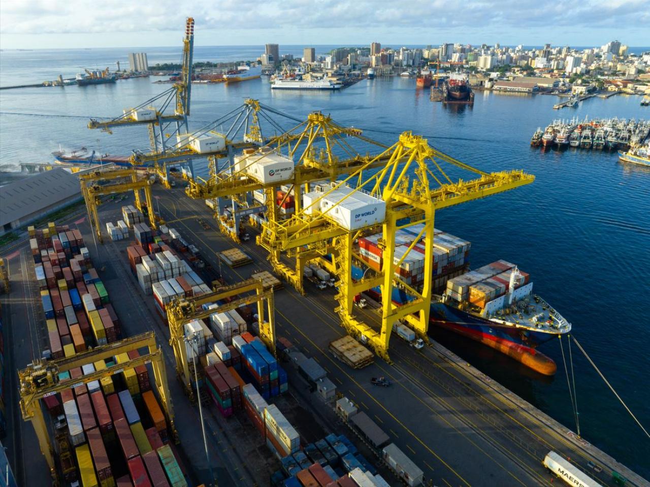Aerial view of DP World’s container terminal at the Port of Dakar, Senegal, showing yellow gantry cranes loading cargo ships and colorful containers along the quay, with the city skyline in the background.