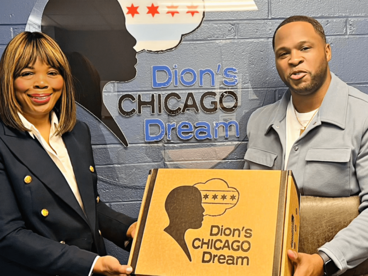 Two people holding a box "Dion's Chicago Dream" on the front and on the wall behind them.