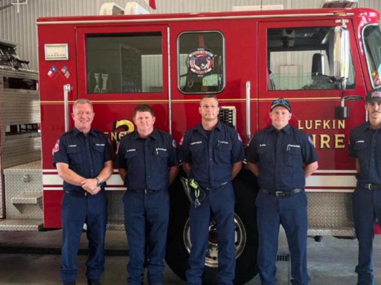 A row of people, some in uniform, in front of a fire truck.