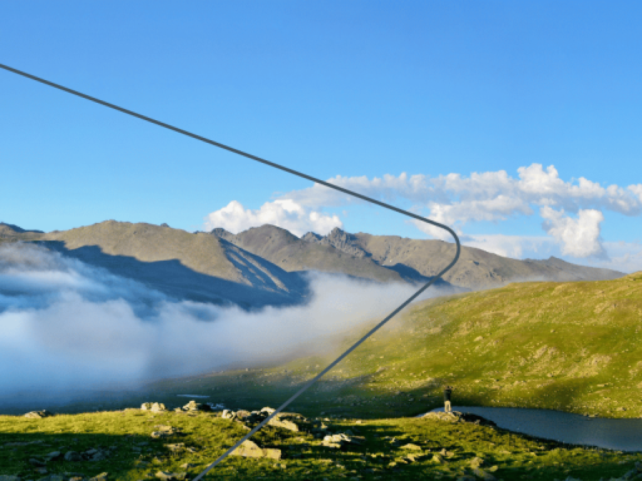 Panoramic view of hills and fog running through the valleys. A blue sky above with very few clouds.