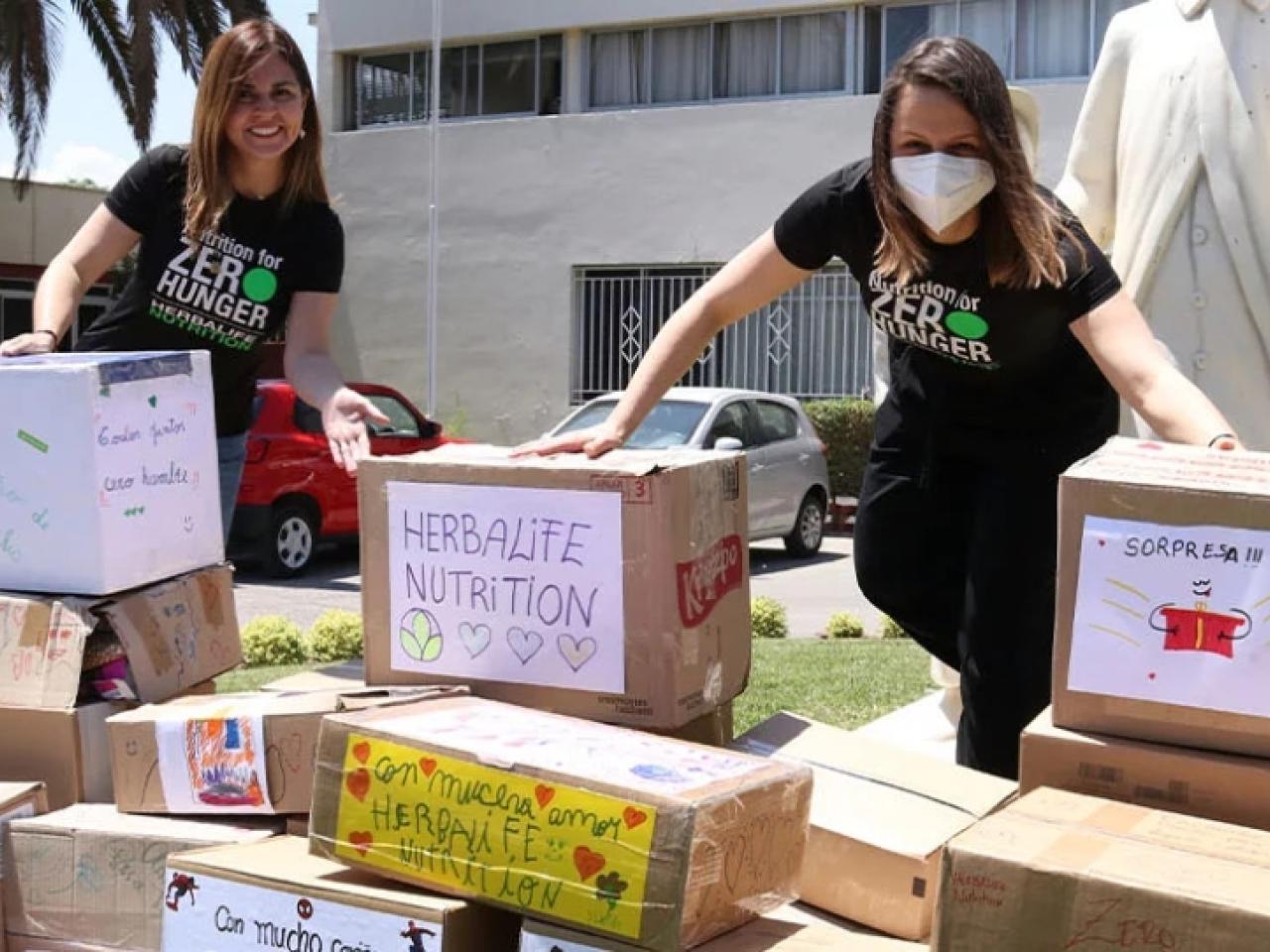 Two volunteers stand outside behind many stacked and hand decorated boxes