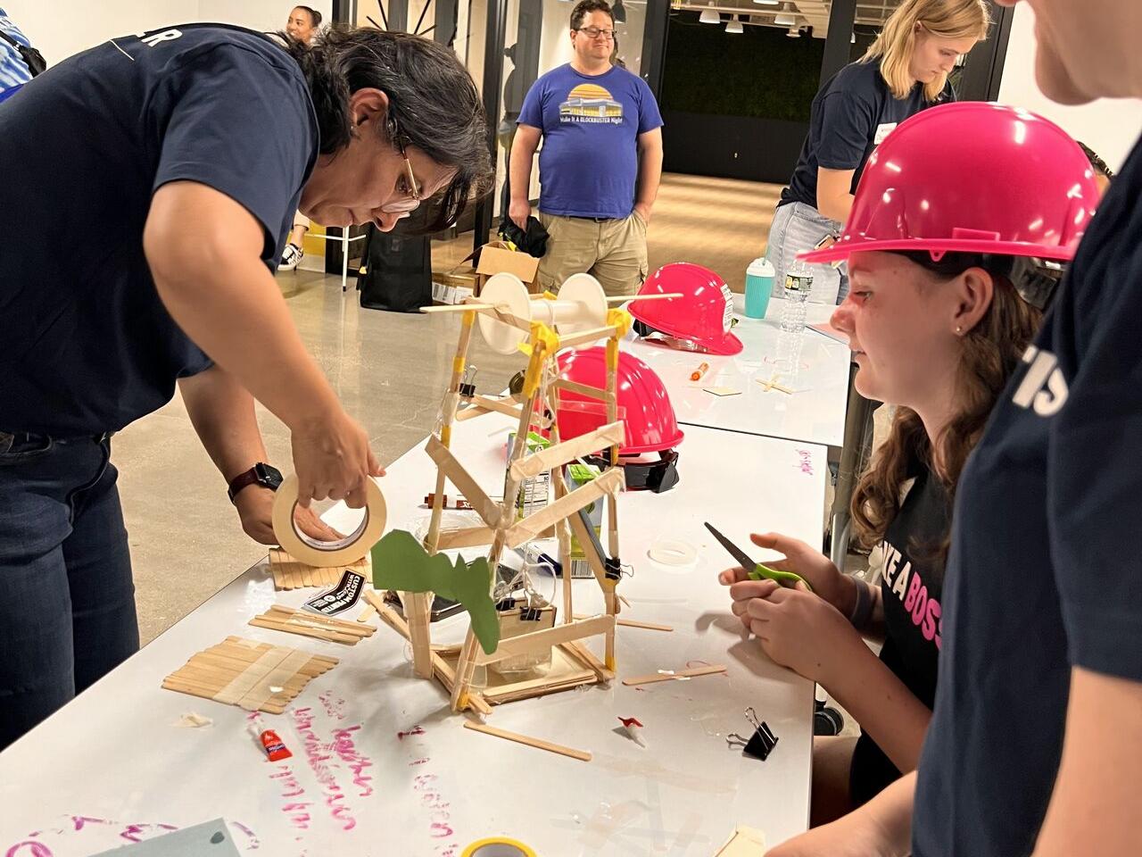 Adult volunteers and children working on building model structures with craft supplies.