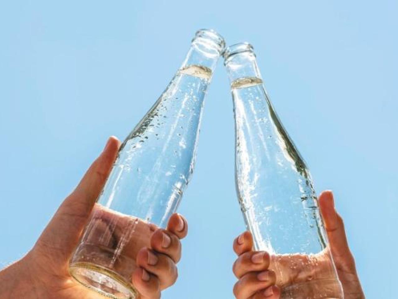 Two hands holding glass bottles, touching at the tops.