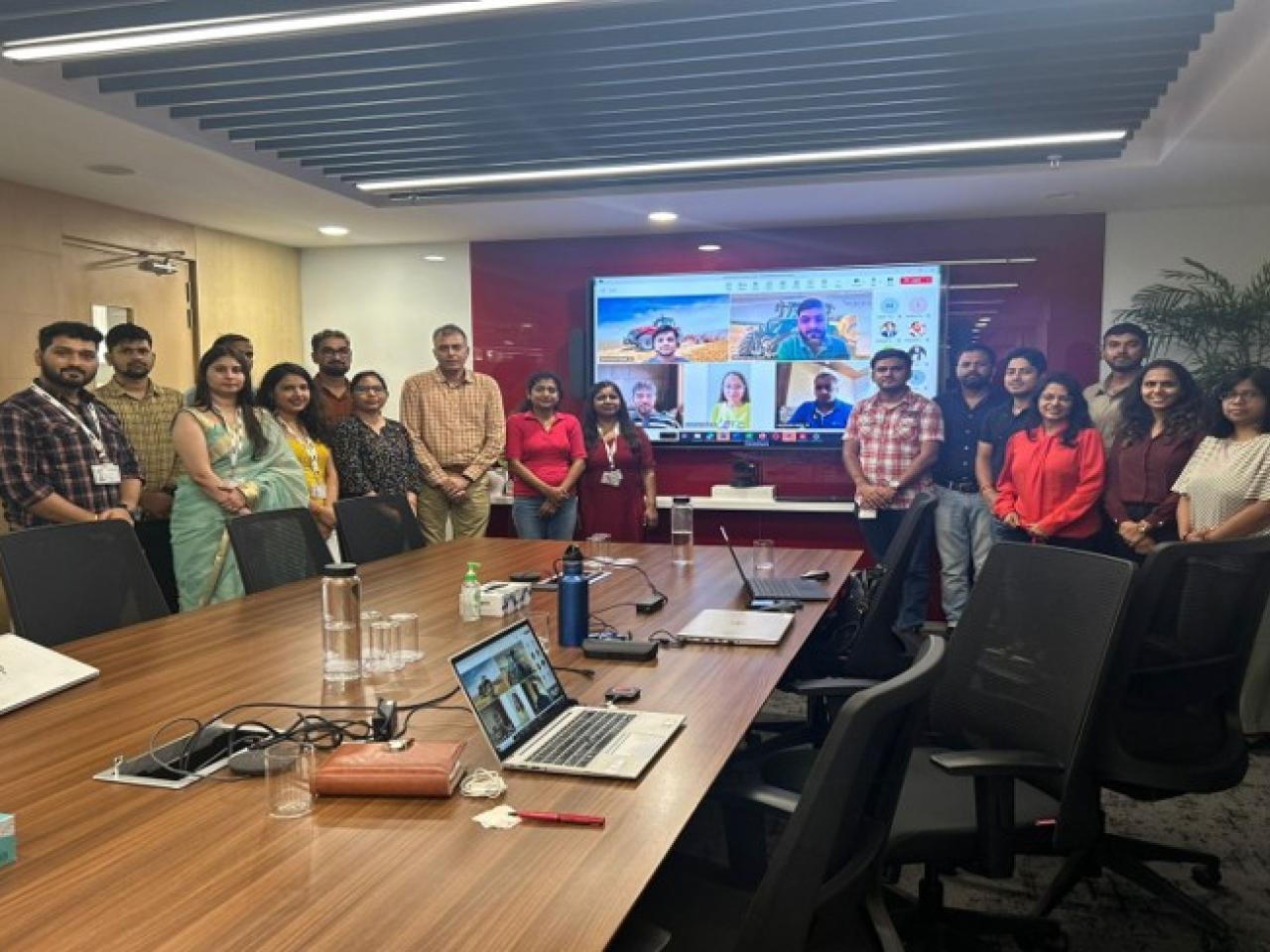 A group of people smiling and standing together in a board room in front of a large screen