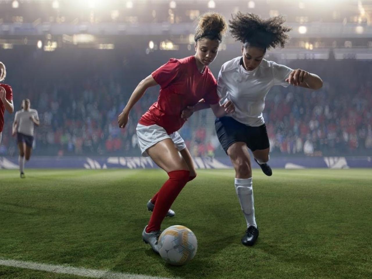 Female soccer players competing for the ball in a game.