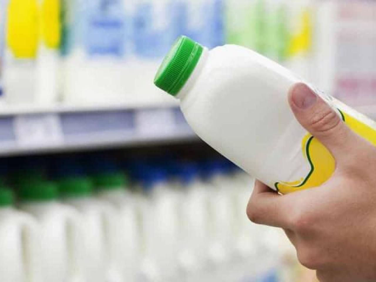A person in a grocery store looking at a plastic container full of white liquid.