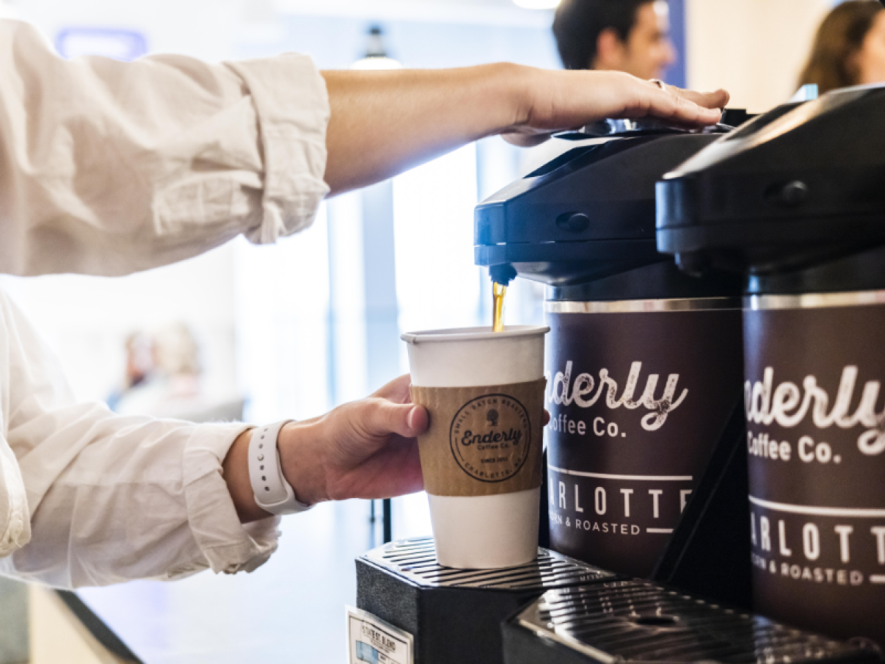 A person getting a cup of coffee from a carafe