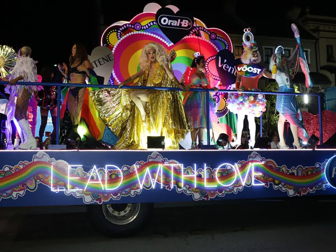 People riding on a pride float with glowing lights that read "Lead with love"