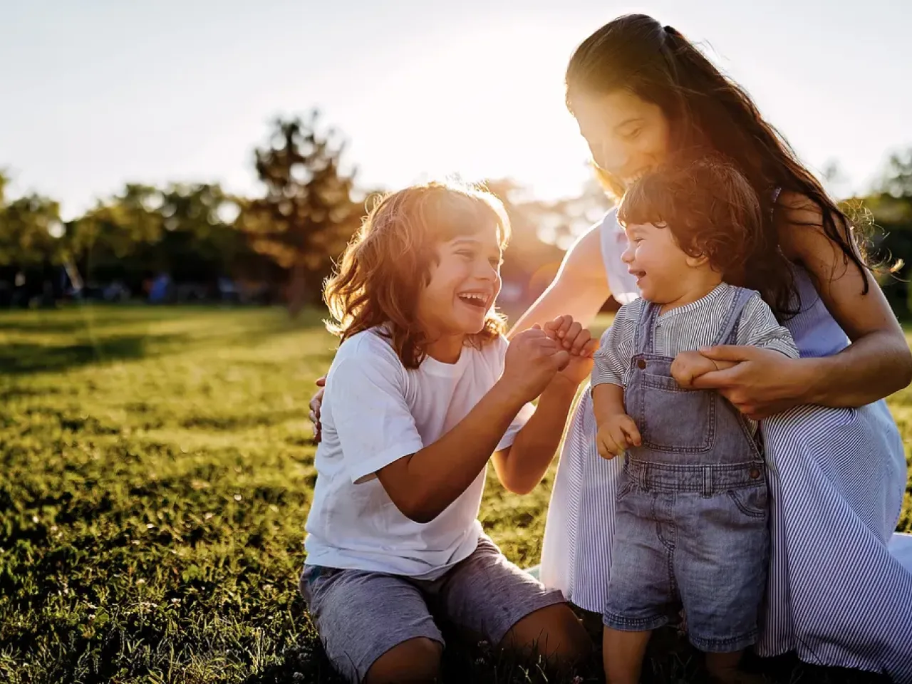 An adult and two children laughing, in an outdoor setting.