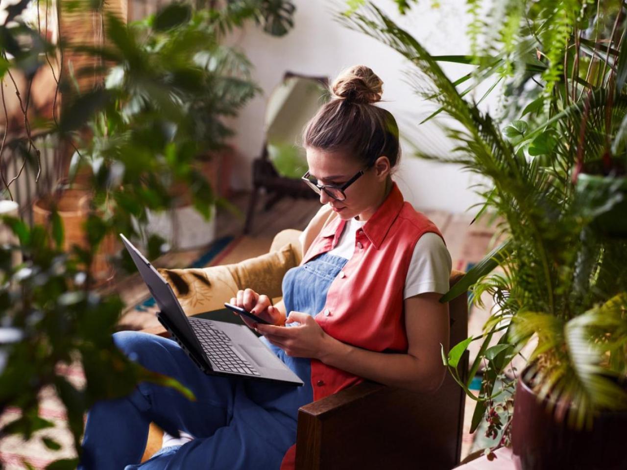Woman working on laptop surrounded by houseplants