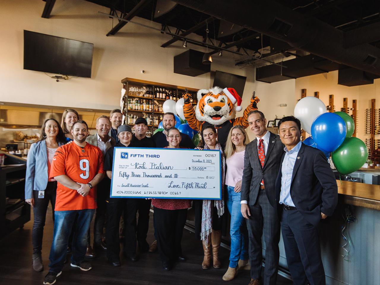 A group posed in a restaurant with a large check. A tiger mascot behind them.