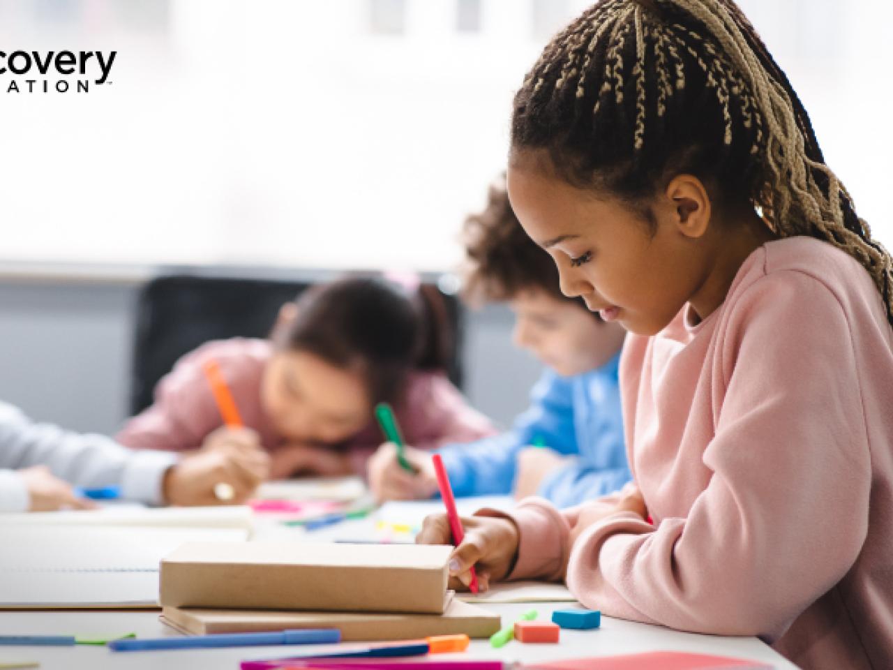 A child writing at a table with other children