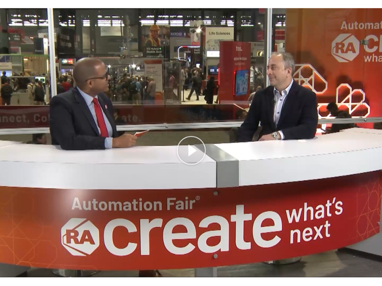 Two people talking behind a desk that reads "Automation Fair: Create what's next"